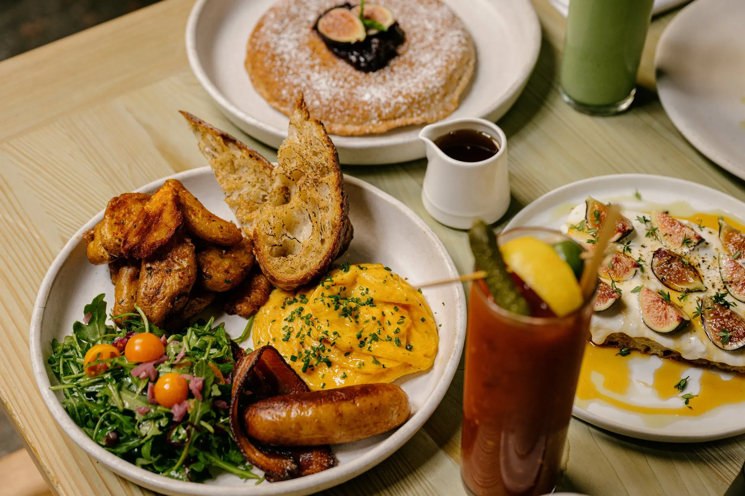 Breakfast table with eggs, potatoes, pancake, figs, and various drinks.