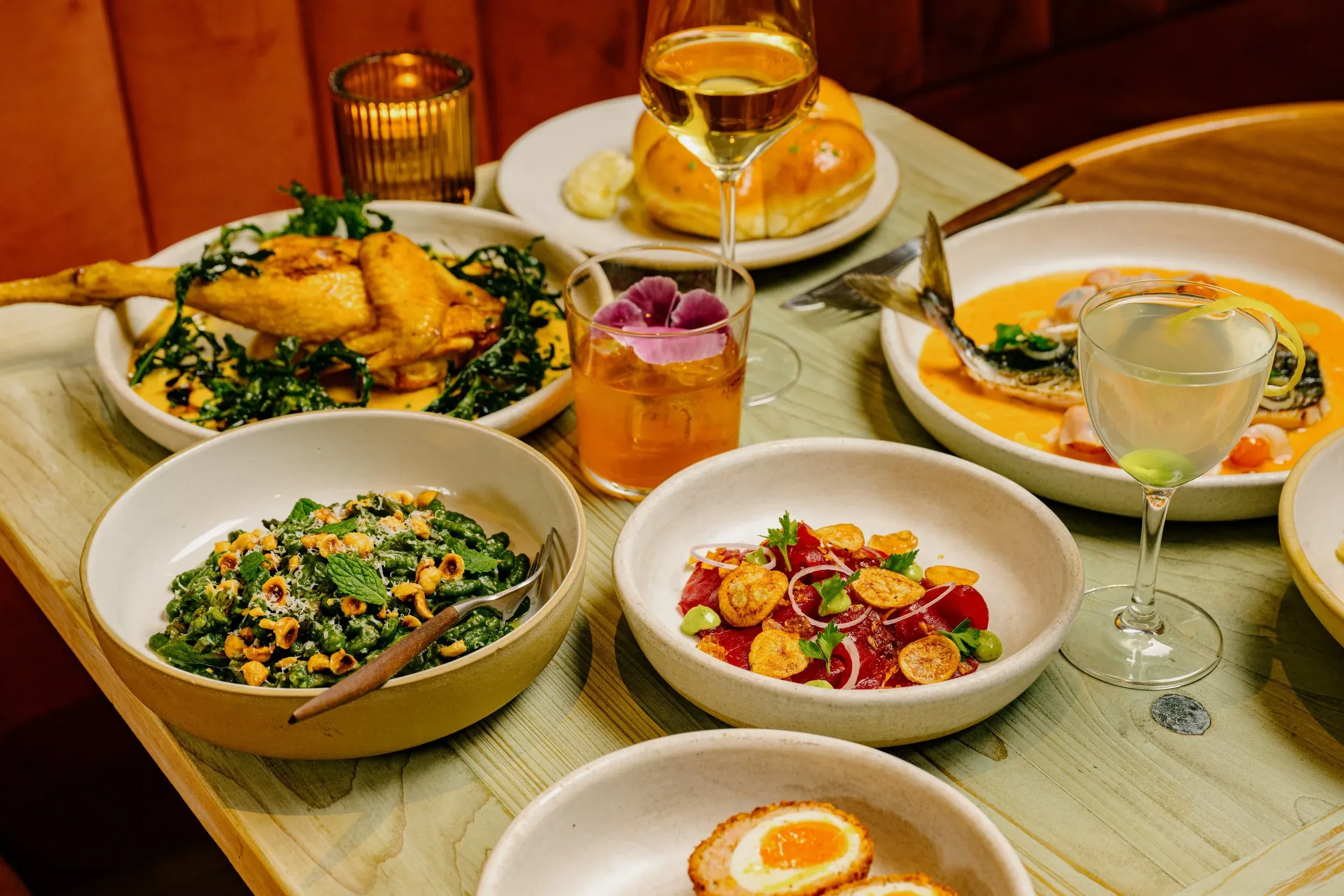 A table with various gourmet dishes, cocktails, and a candle.