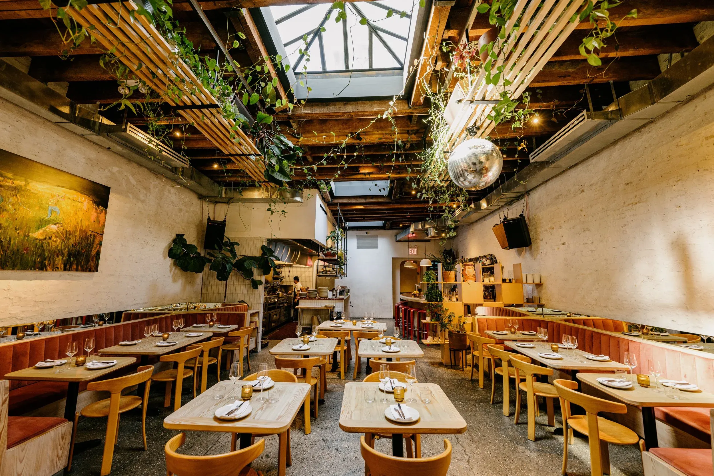 Modern restaurant interior with wooden tables, upholstered banquettes, and hanging plants.