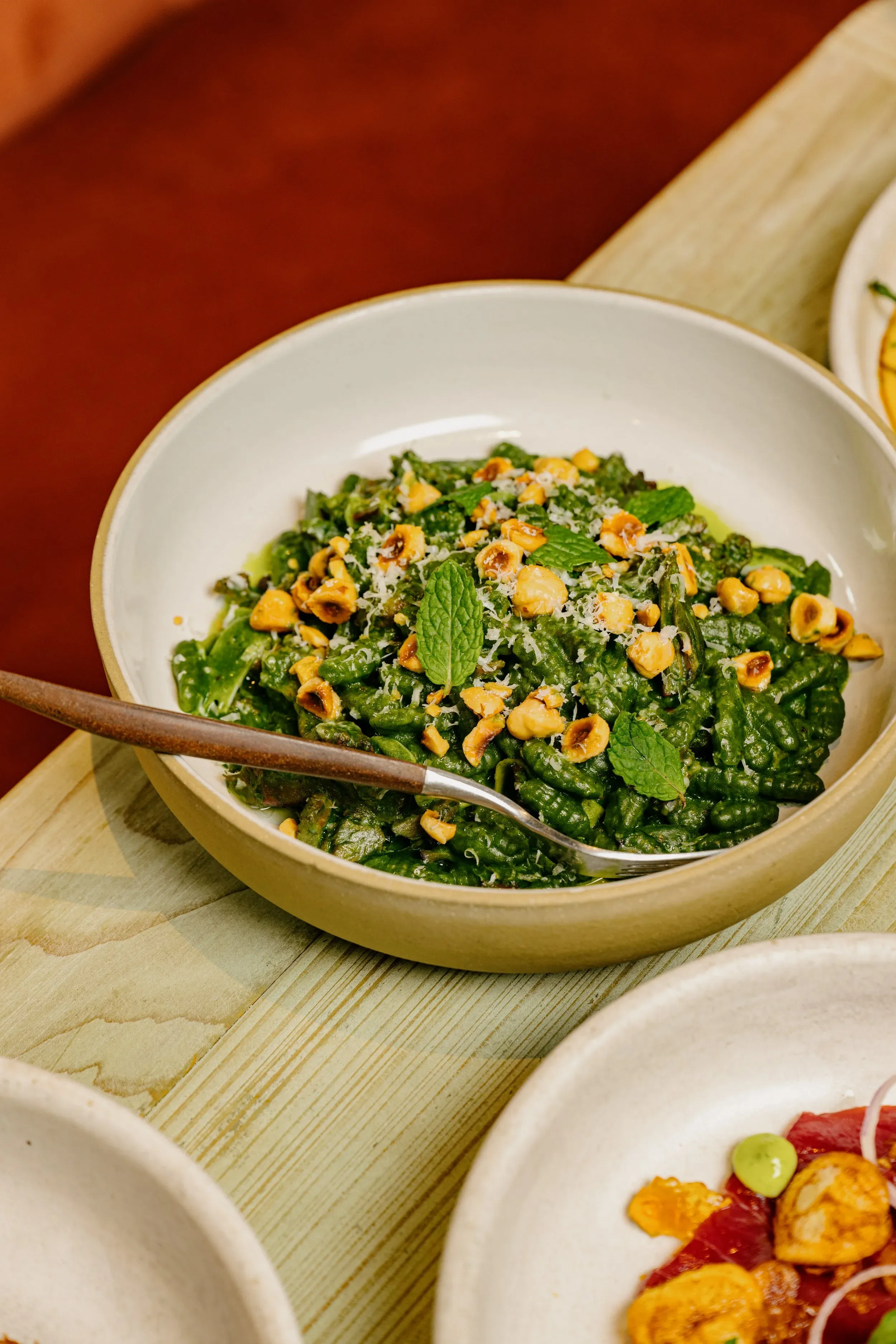 Green pasta dish with hazelnuts, grated cheese, and mint leaves.