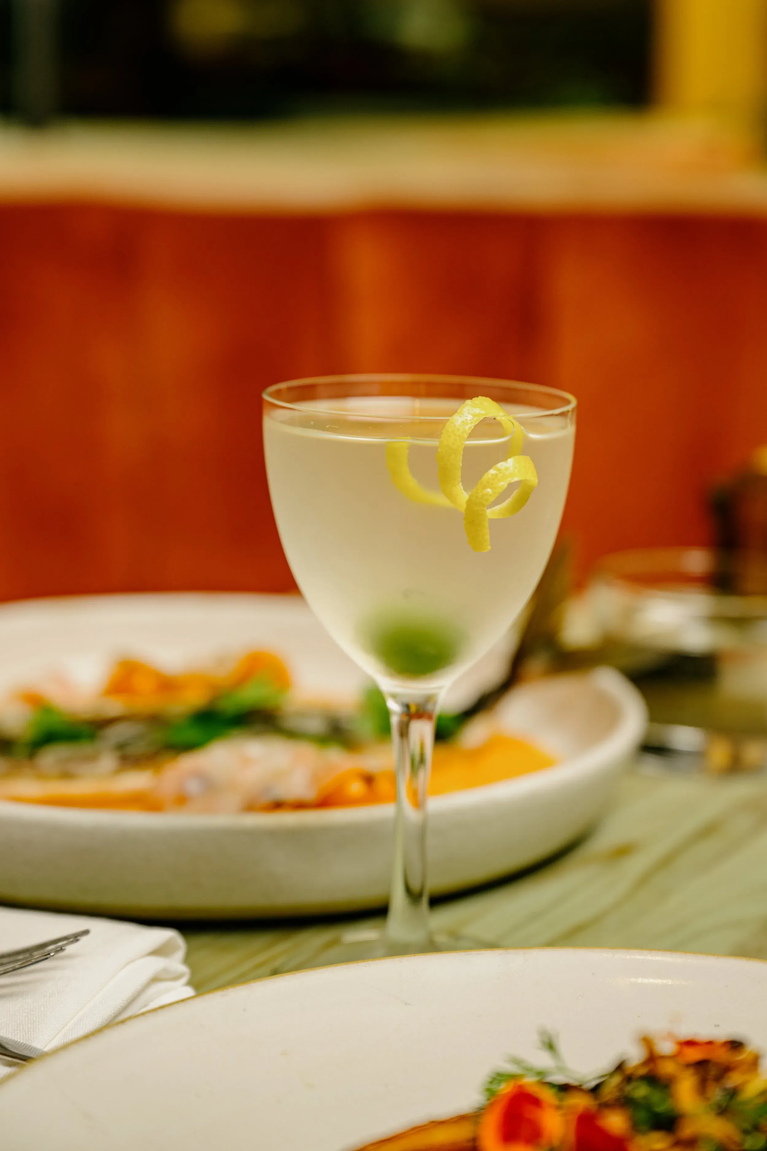 A drink with a lemon peel and olive on a restaurant table.