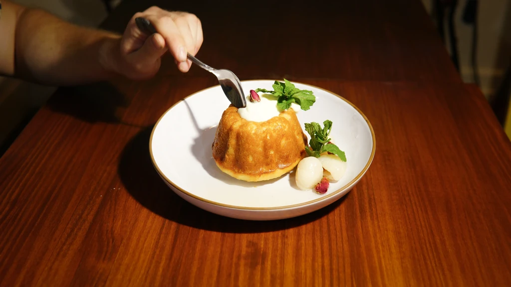 Person spoons cream from a cake, with lychees and mint.
