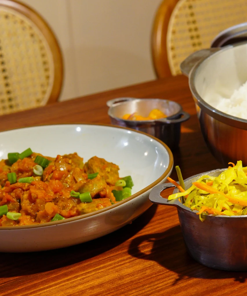 A bowl of curry, rice, and two side dishes on a wooden table.