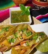 Three tacos, salsa verde, and lime wedge on a white plate.