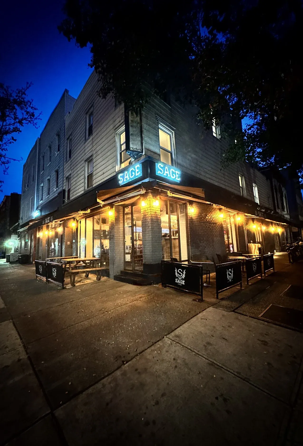 A dark night view of the Sage restaurant with lit signs.