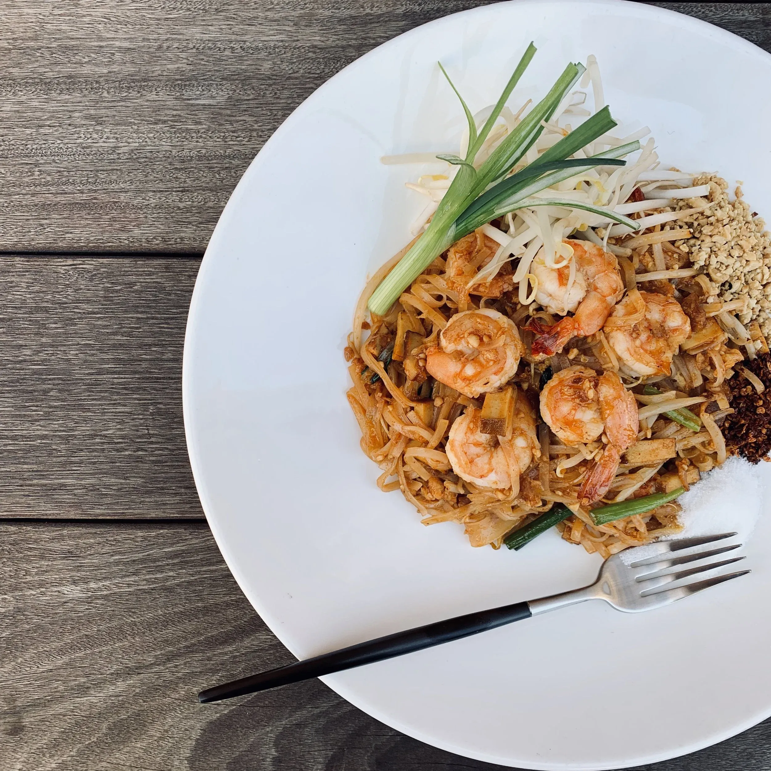 Pad Thai with shrimp, sprouts, peanuts, and a fork on a white plate.