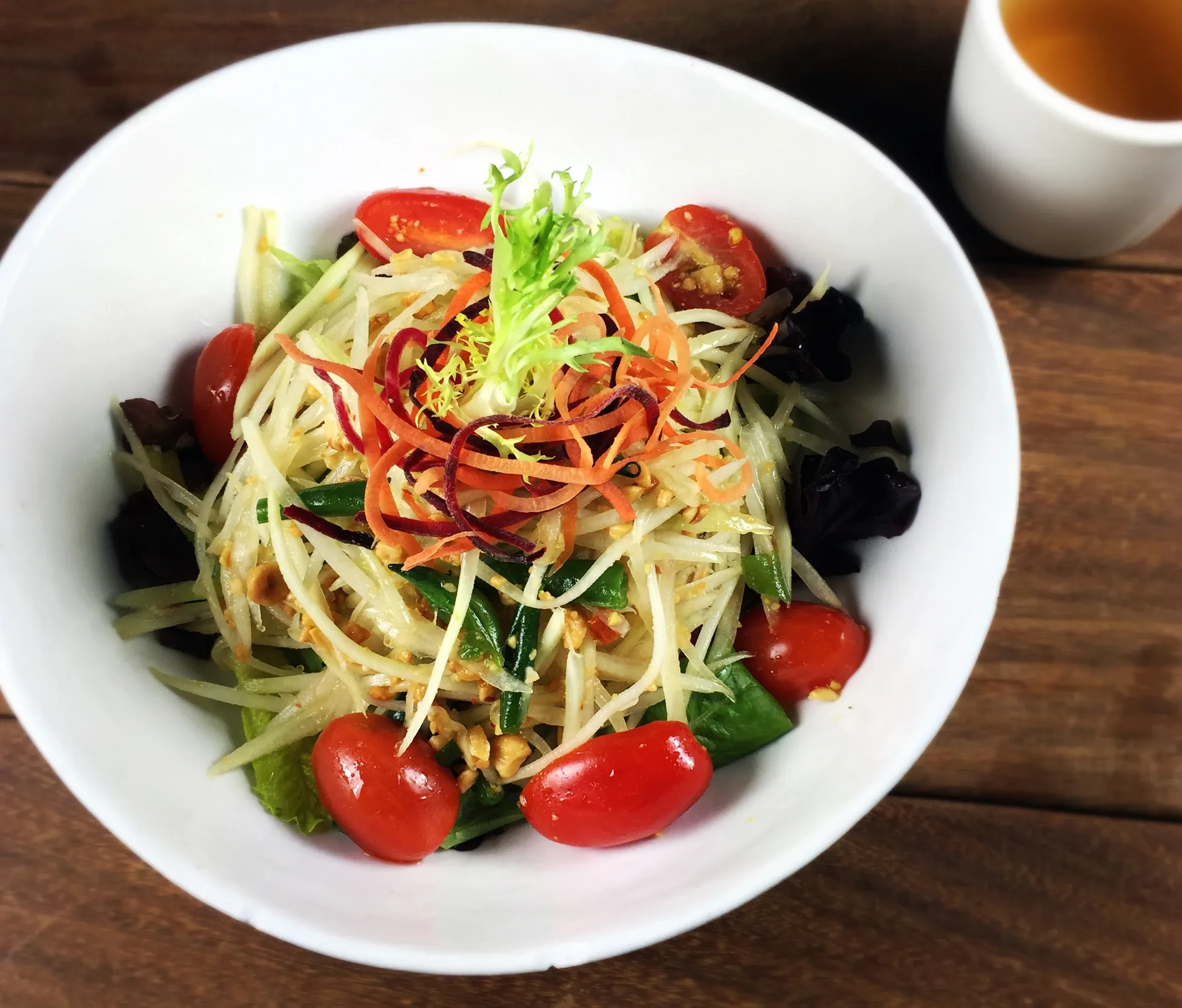 Green papaya salad with tomatoes and peanuts in a white bowl.