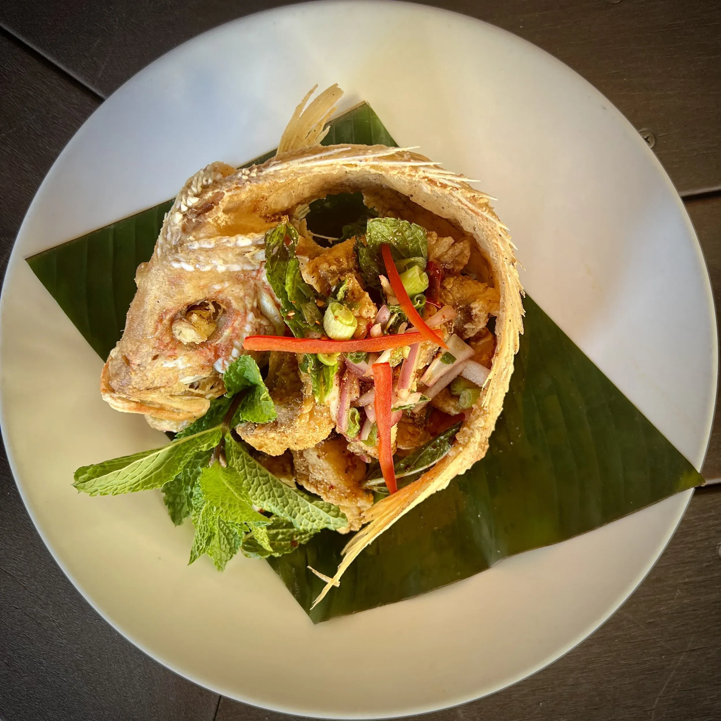 Crispy fried fish with fresh herbs, chili, and lime on a banana leaf.