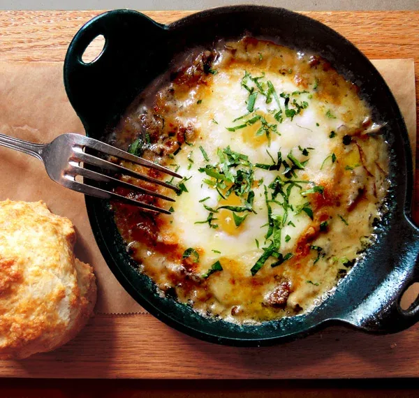 Baked eggs with cheese and herbs in a skillet, with a biscuit.