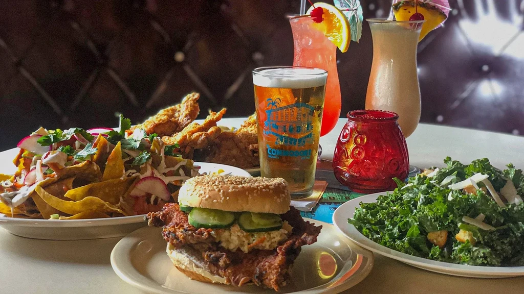 A table spread with nachos, fried chicken, a sandwich, salad, beer, and cocktails.