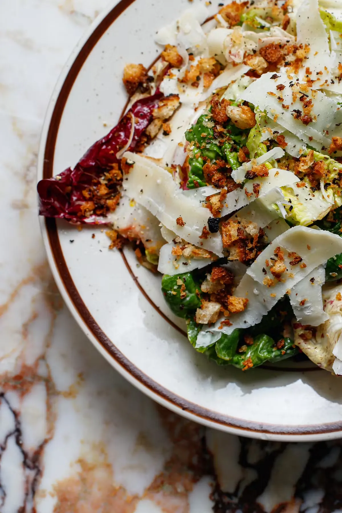 Close-up of Caesar salad with radicchio, cheese, and croutons on white marble.