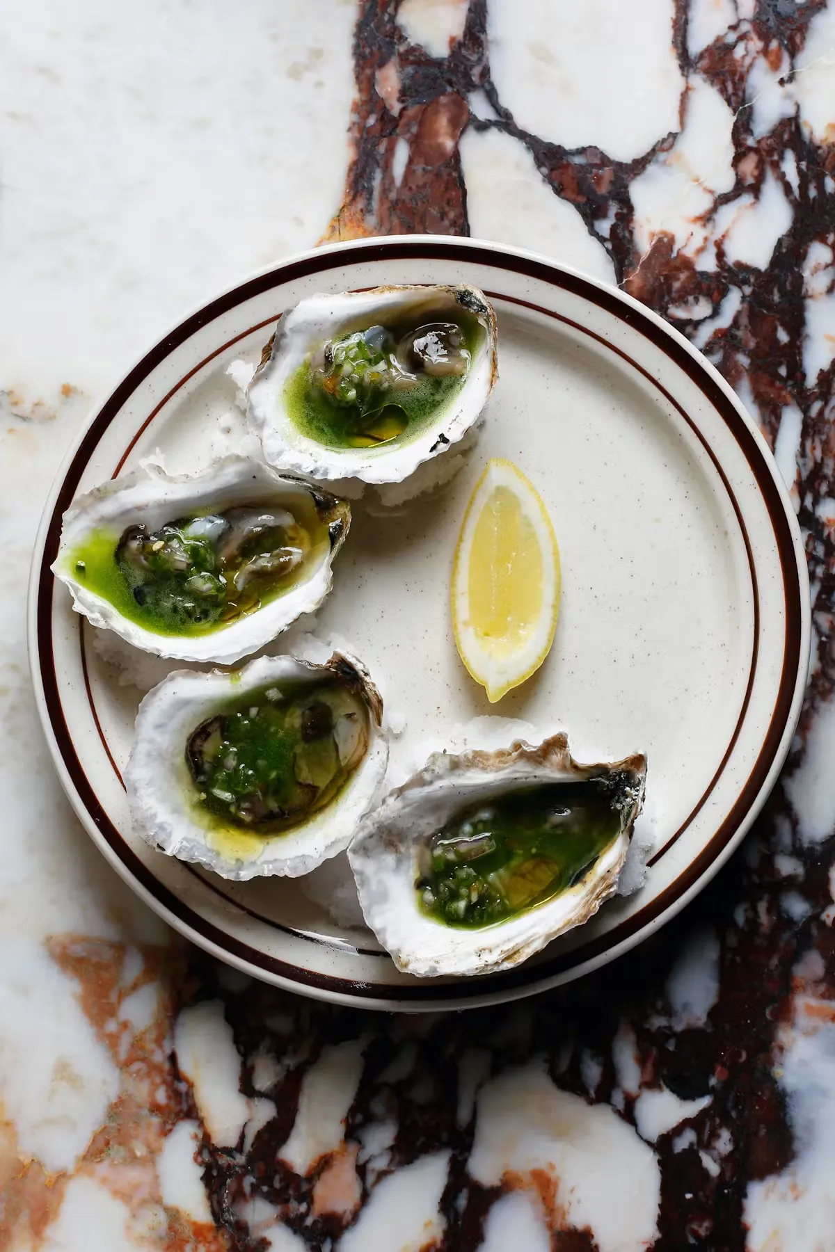 Four oysters with green sauce and lemon on a plate.