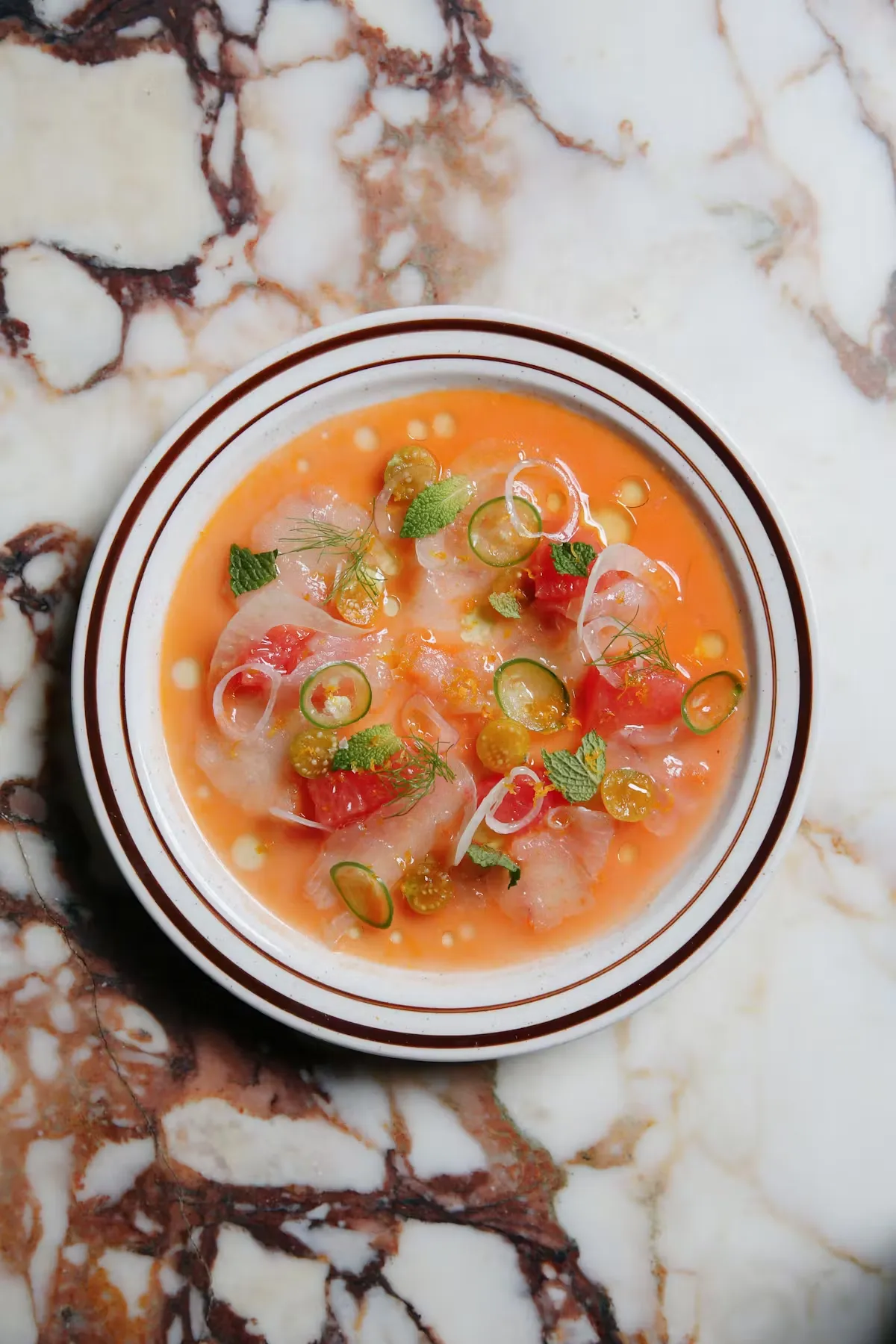 White fish crudo in orange sauce with mint and grapefruit on marble.