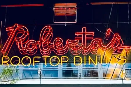 Neon sign for "Roberta's Rooftop Dining" in red and yellow.