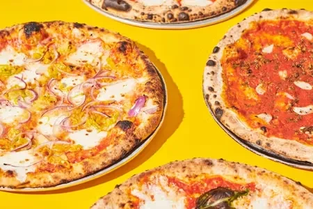 Four pizzas with different toppings on a bright yellow background.