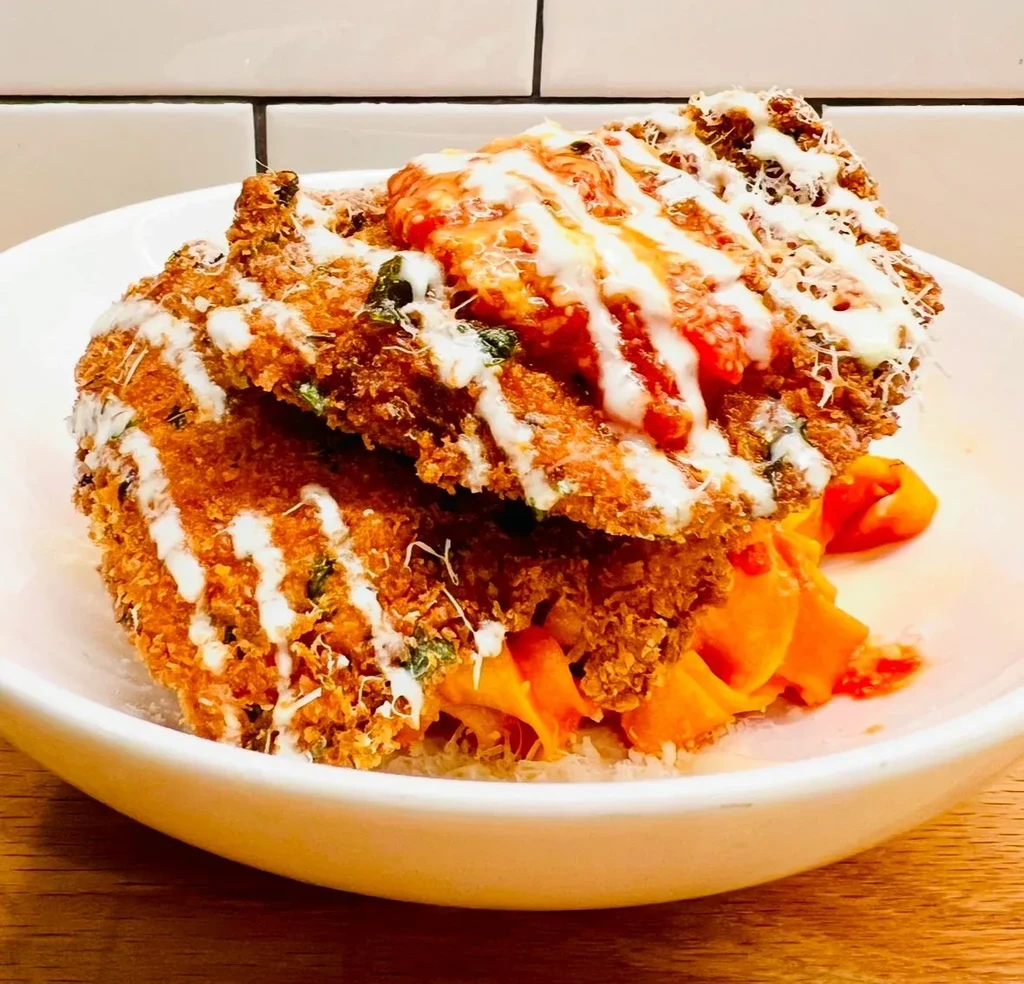 Two breaded chicken cutlets topped with sauce, cheese, and pasta.