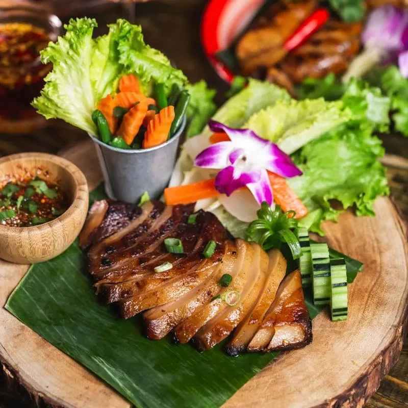 Grilled pork slices with vegetables, dipping sauce, and an orchid.