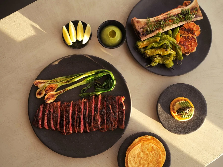 A table with various plates of sliced steak, bone marrow, and appetizers.