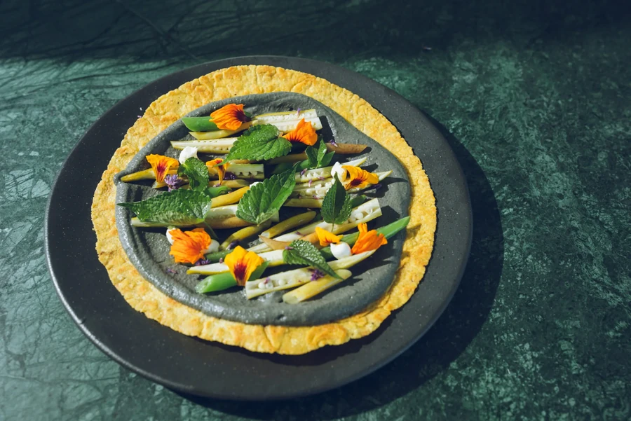 A savory tart with vegetables, edible flowers, and fresh mint on a plate.