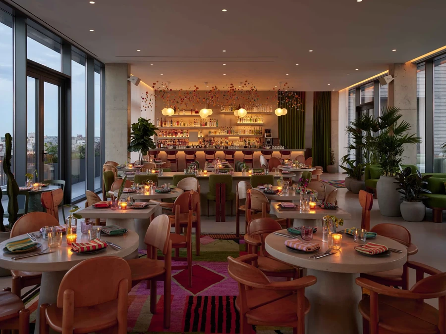 Modern restaurant interior with floor-to-ceiling windows, bar, and colorful decor.