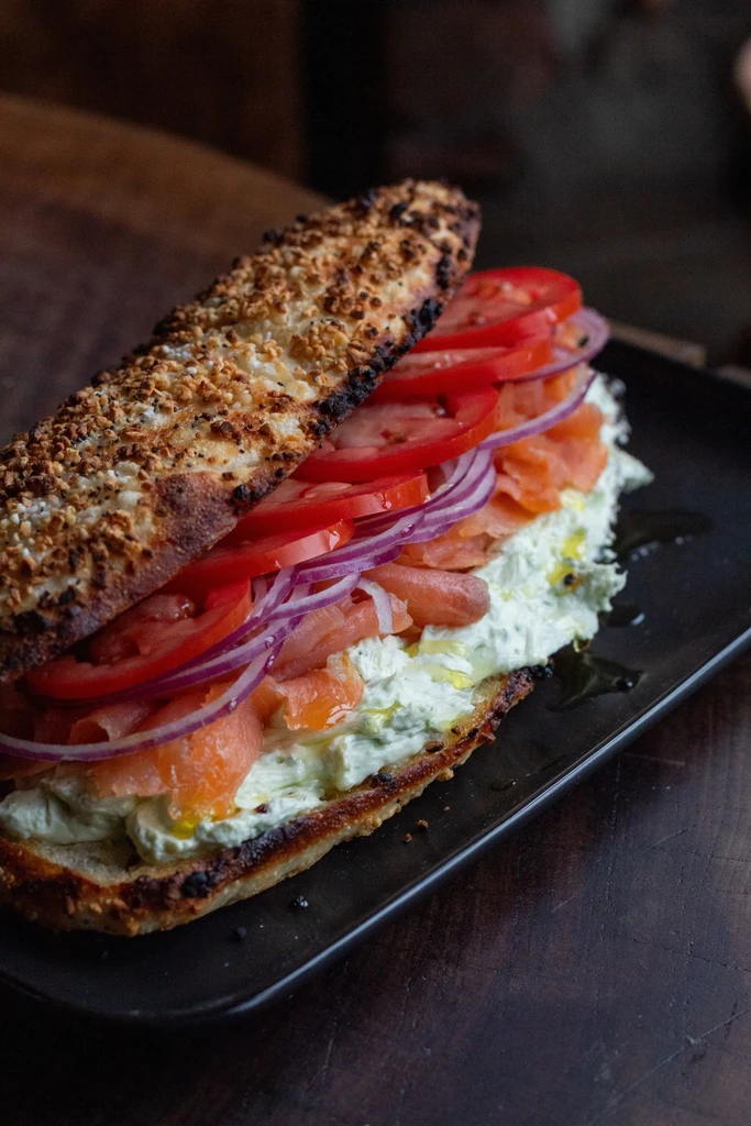 A toasted baguette sandwich with cream cheese, smoked salmon, tomatoes, and red onions.