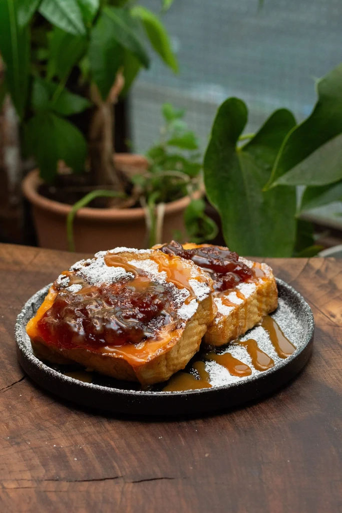 Two French toast slices with jam, caramel, and powdered sugar on a plate.