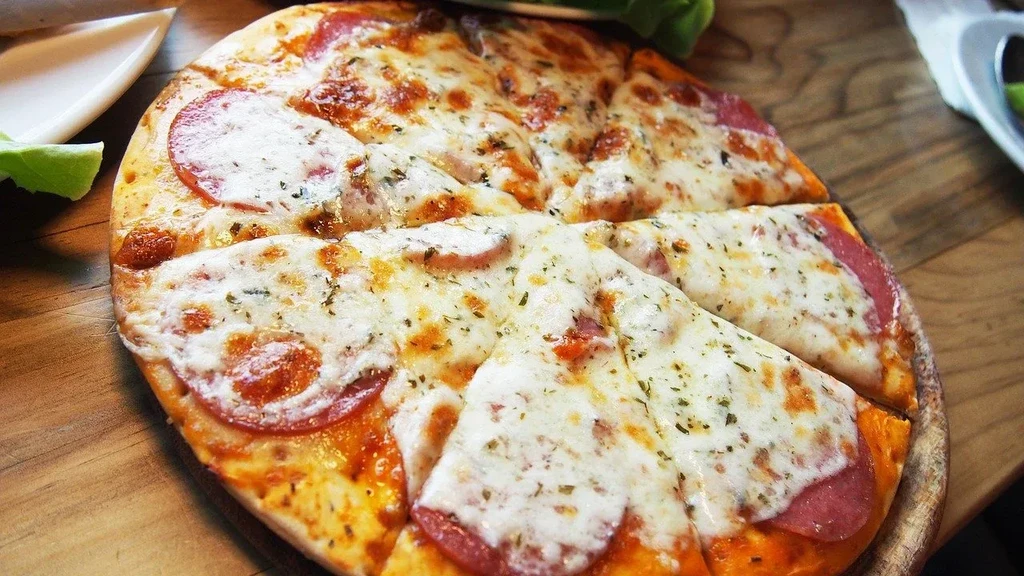 A sliced pepperoni pizza with melted cheese and herbs on a wooden board.