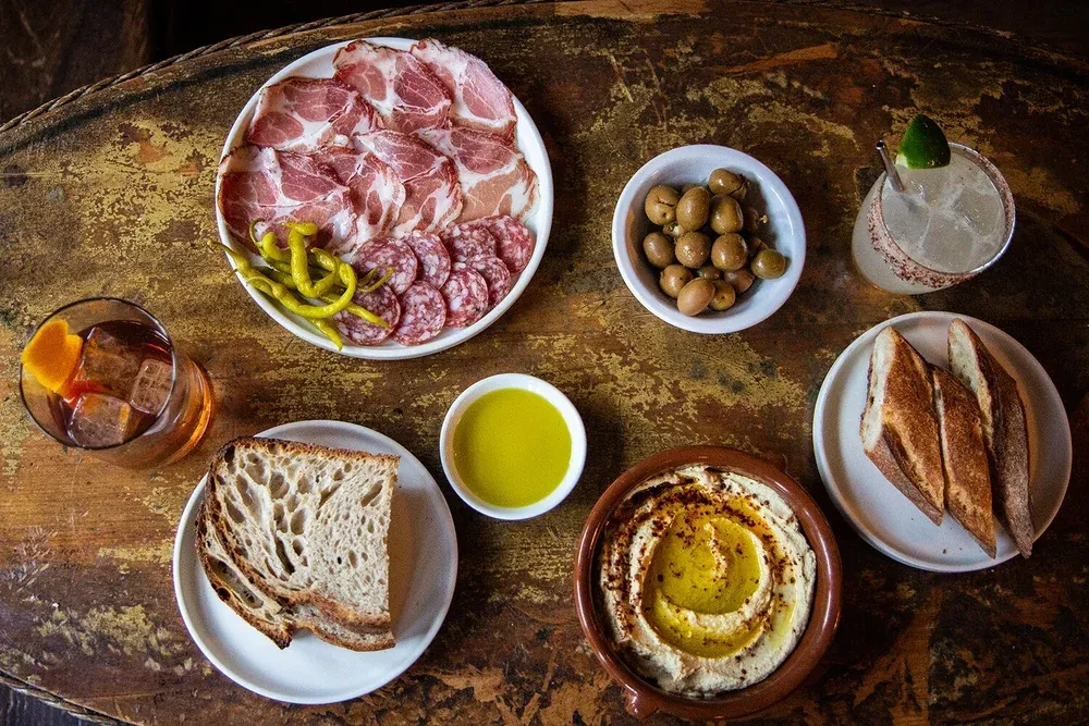 An overhead view of a charcuterie board with drinks, hummus, and bread.