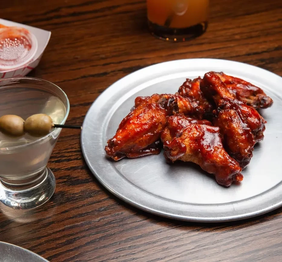 Chicken wings on a metal plate next to a martini with olives.