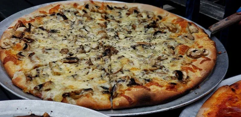 A large mushroom pizza with white cheese on a metal pan.