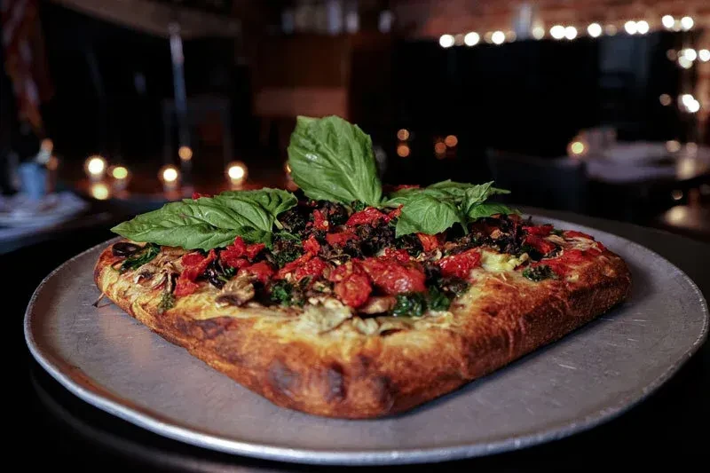 Square pizza with basil leaves and tomatoes on a metal pan.