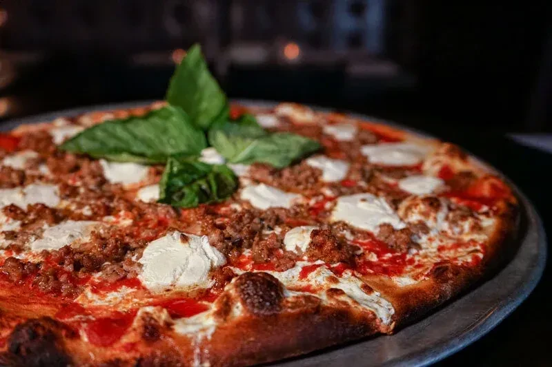 A whole pizza with sausage, ricotta, red sauce, and basil on a metal tray.
