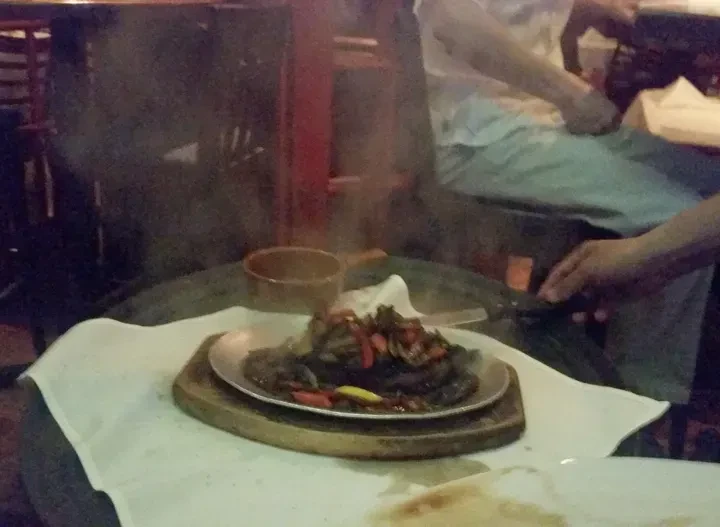 Sizzling steak and vegetables are served on a hot plate at a restaurant.