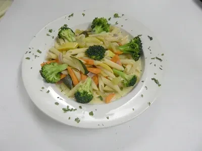 Penne pasta with broccoli, carrots, and zucchini on a white plate.