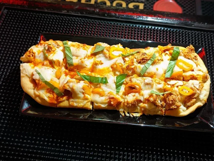 Long rectangular flatbread pizza with melted cheese, chicken, basil, and peppers.