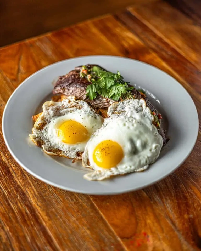 Steak and two fried eggs on a white plate.