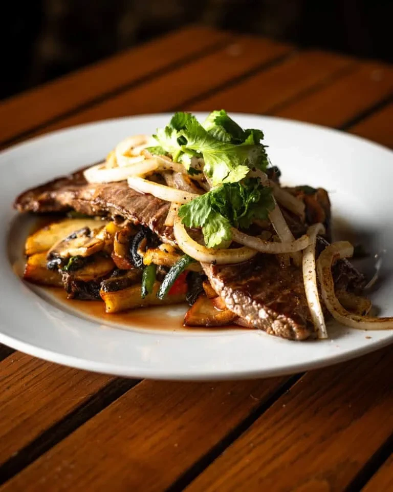 Steak with sauteed vegetables, onions, and cilantro on a white plate.