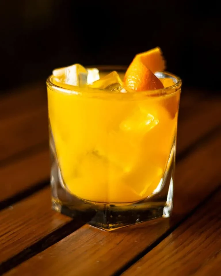 An orange drink with ice and an orange peel on a wooden table.