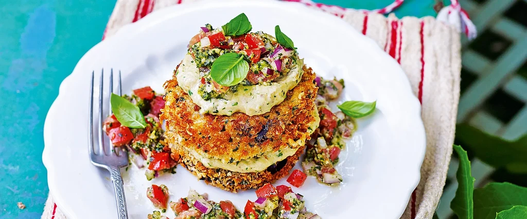 Stacked fritters topped with salsa, hummus, and basil on a white plate.