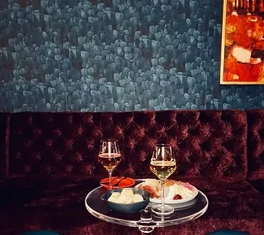 A tray with two wine glasses and snacks on a velvet couch.