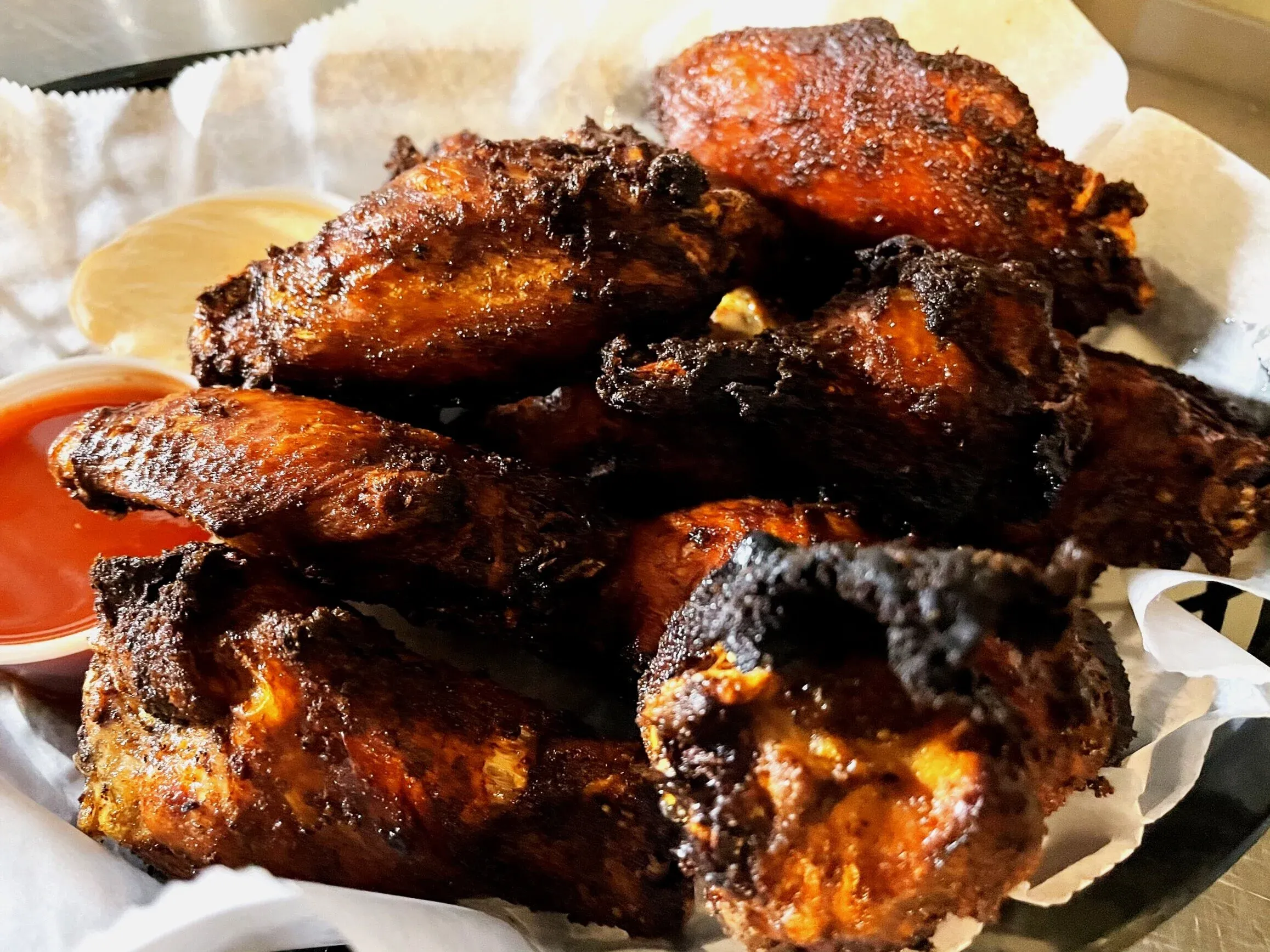 Close-up of a basket of crispy fried chicken wings with two dipping sauces.