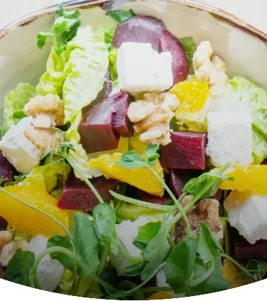 A bowl of vibrant salad with lettuce, beets, feta, walnuts, and oranges.
