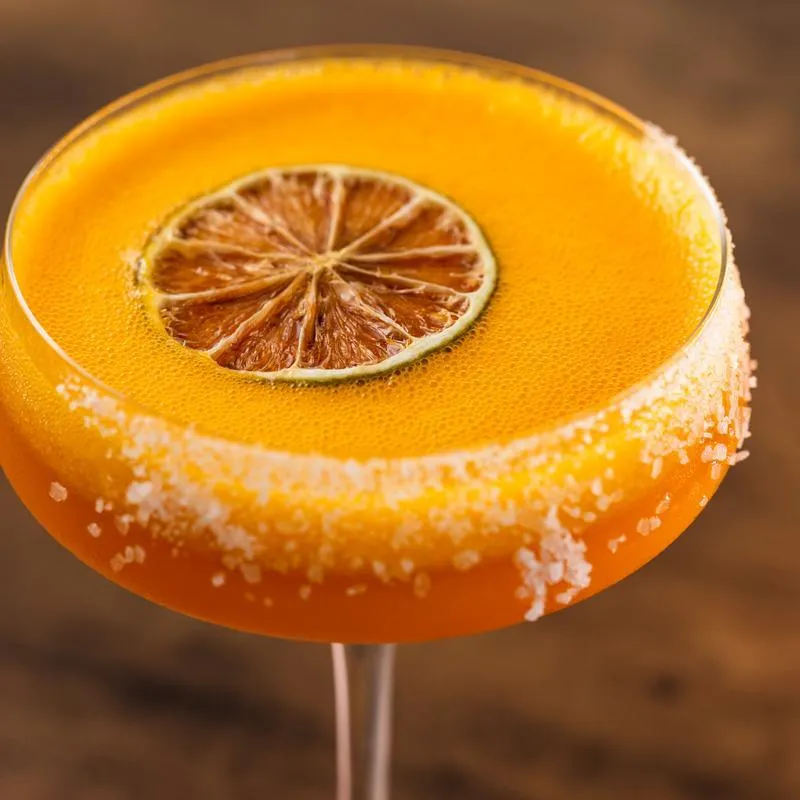 Orange cocktail with a dried lime slice and salt on the rim.