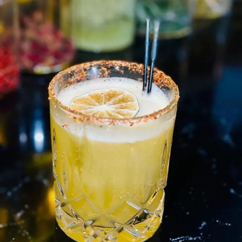 Yellow cocktail with foam, dried lime, and a spiced rim.