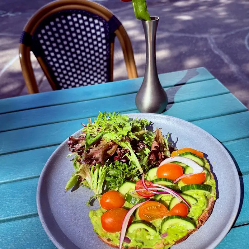 Avocado toast with salad on a blue table at an outdoor cafe.