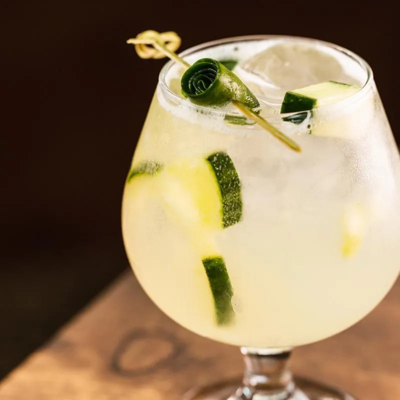 A goblet of light-colored drink with cucumber slices and ice.