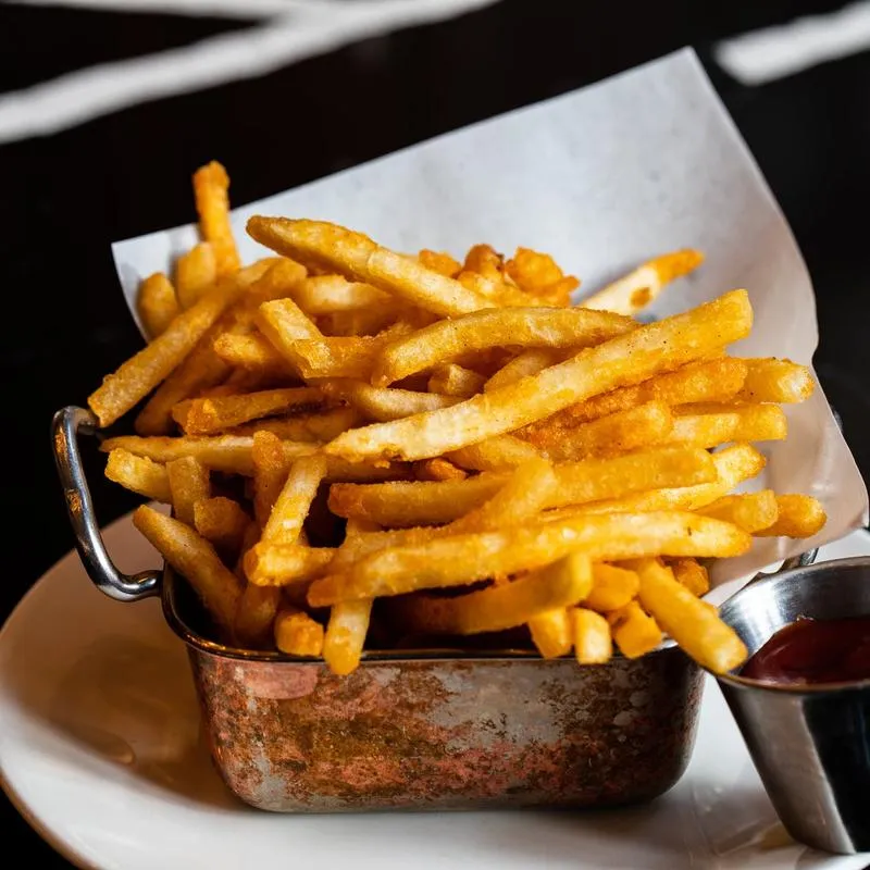 Golden french fries in a metal basket with ketchup.
