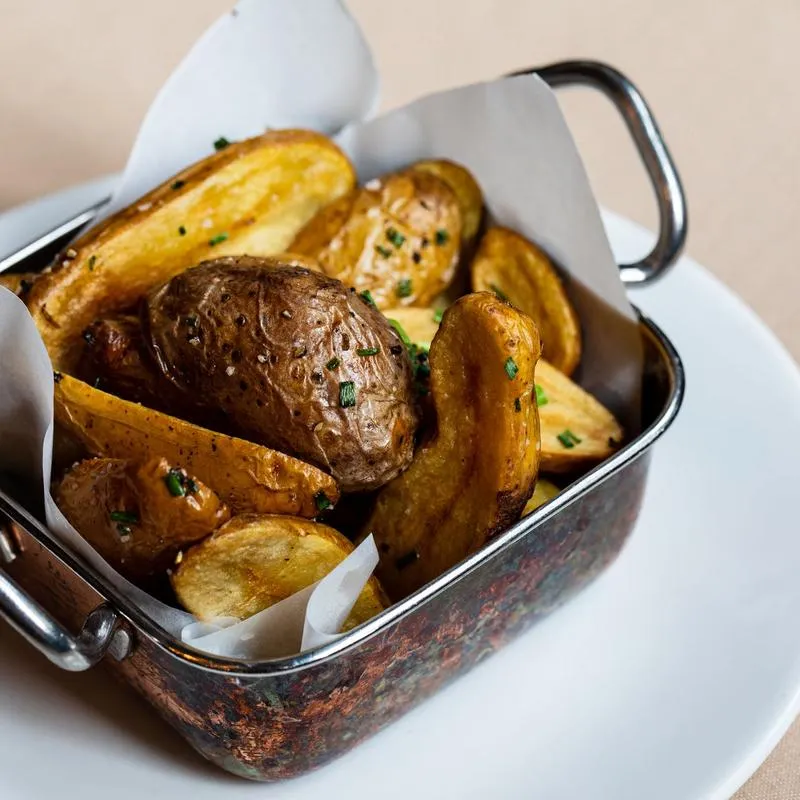 Baked potatoes and potato wedges with chives in a metal basket.