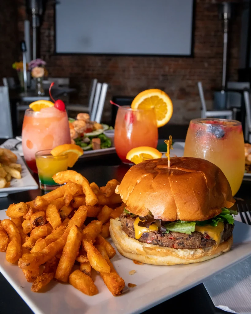 A plant-based burger and fries next to tropical drinks on a black table.