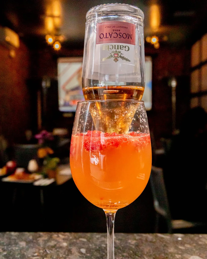 An upside-down Moscato bottle inside a wine glass with a cocktail.